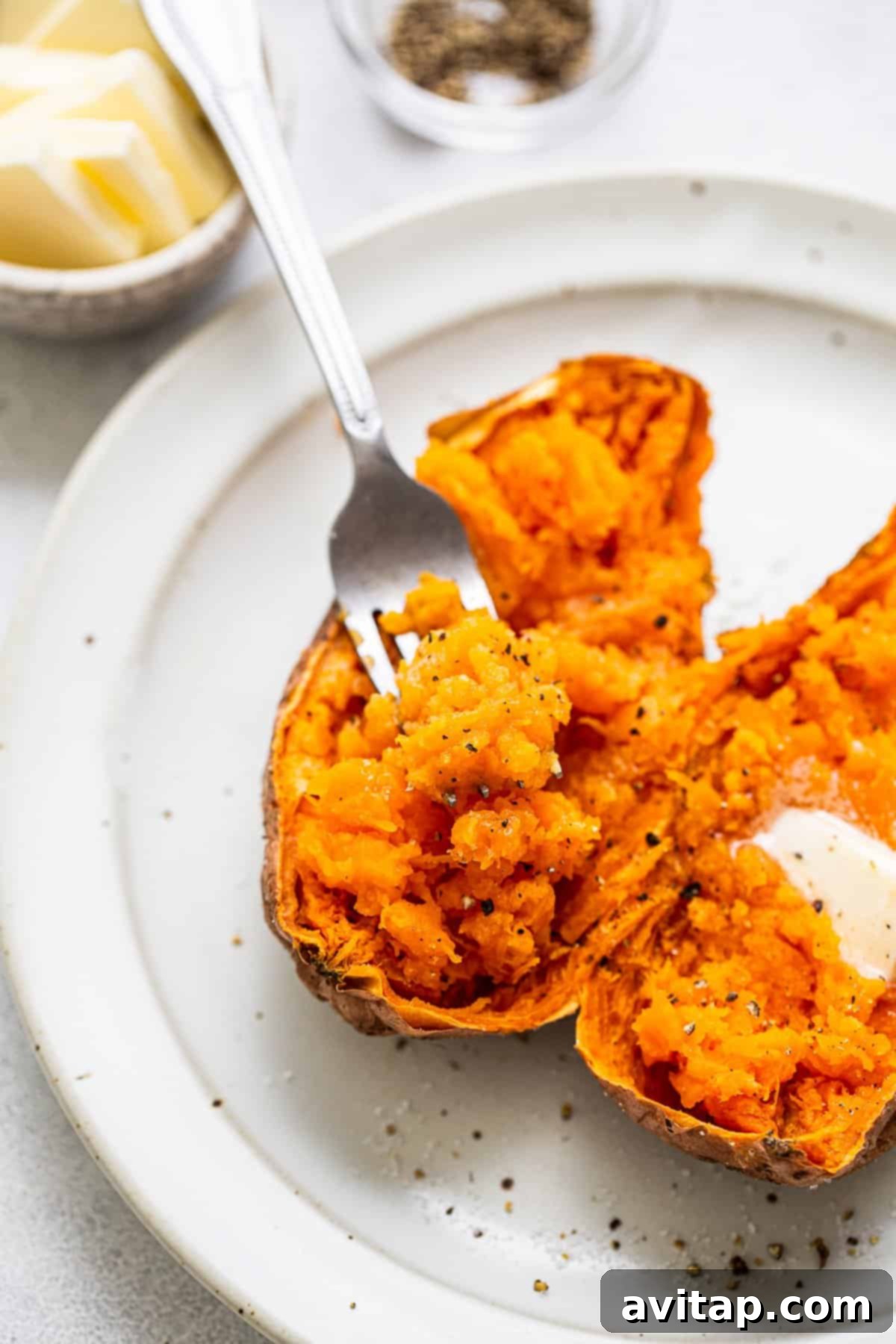 A fork scooping out the fluffy, orange middle of a perfectly cooked sweet potato on a plate, emphasizing its tender texture.