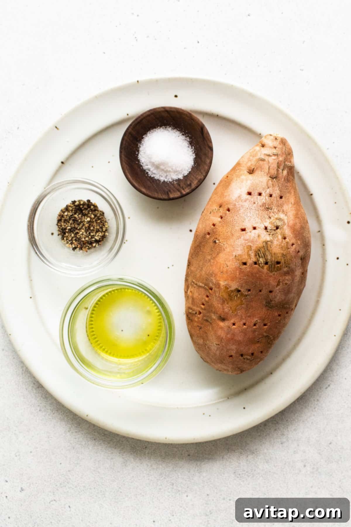 A simple arrangement of a raw sweet potato, a salt shaker, a pepper grinder, and a bottle of olive oil on a plate, highlighting the minimal ingredients needed.