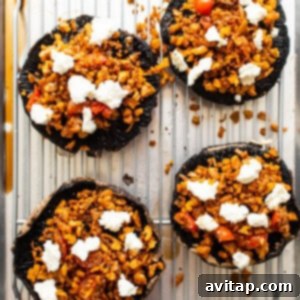 Stuffed portobello mushrooms topped with goat cheese, ready for broiling.