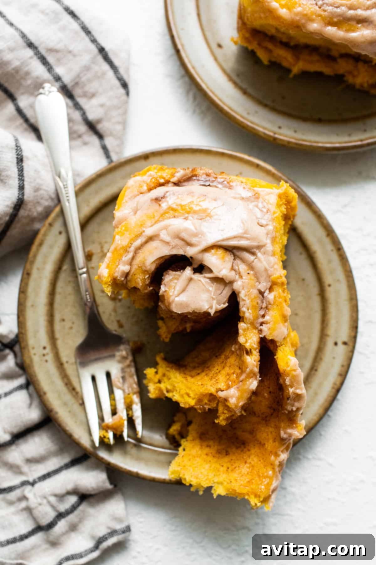 Indulge in these delicious pumpkin cinnamon rolls with a delightful cinnamon cream cheese frosting. Learn how to prepare them overnight for an easy morning bake! A single pumpkin cinnamon roll on a white plate with a fork, showing the generous cinnamon cream cheese frosting and pumpkin-infused dough.