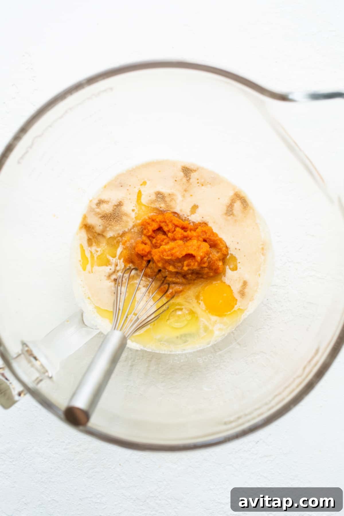 Prepare the vibrant wet ingredients for your homemade pumpkin cinnamon rolls, including pumpkin puree for rich flavor and color. Wet ingredients for pumpkin cinnamon rolls in a bowl, showing the vibrant orange pumpkin puree and other liquids ready to be mixed.