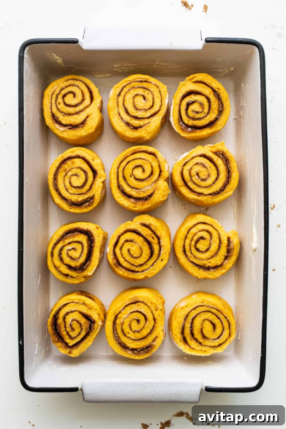 A batch of baked pumpkin cinnamon rolls, perfectly golden and ready for a generous topping of cream cheese frosting. Freshly baked pumpkin cinnamon rolls nestled closely in a baking dish, glistening with warmth and ready for frosting.