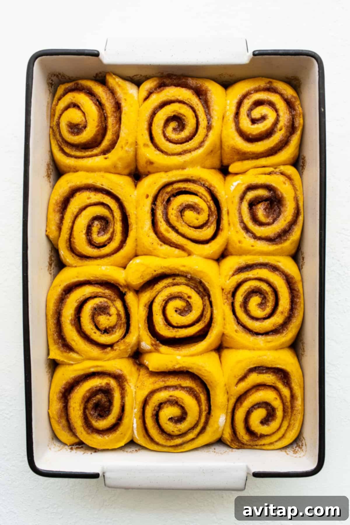 Golden and tender pumpkin cinnamon rolls, a perfect fall treat emerging from the oven. Close-up of golden brown pumpkin cinnamon rolls in a ceramic baking dish, showing the beautiful spirals and tender texture.