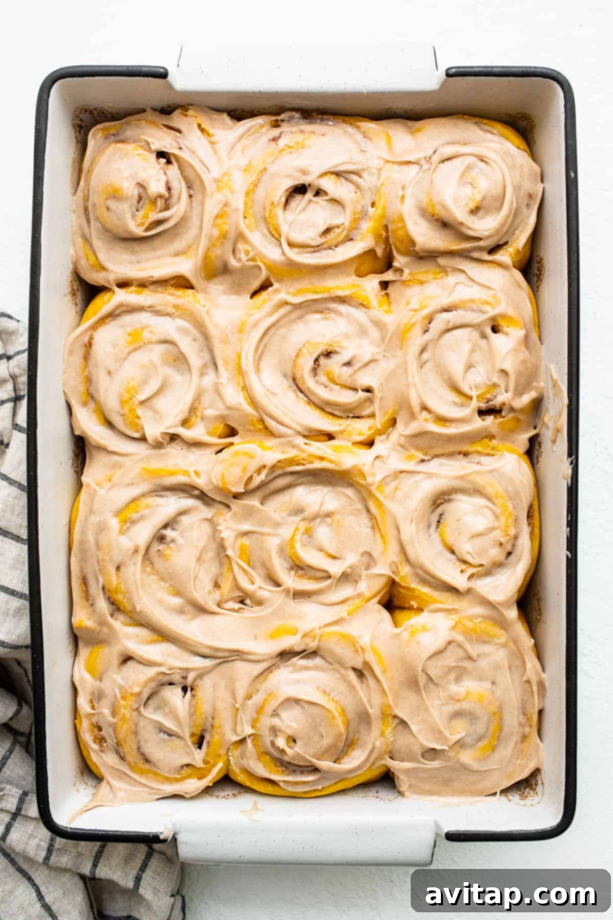 Indulge in these warm pumpkin cinnamon rolls, decadent with cinnamon cream cheese frosting, straight from the baking dish. Warm pumpkin cinnamon rolls generously covered with cinnamon cream cheese frosting in a baking dish, ready to be served.