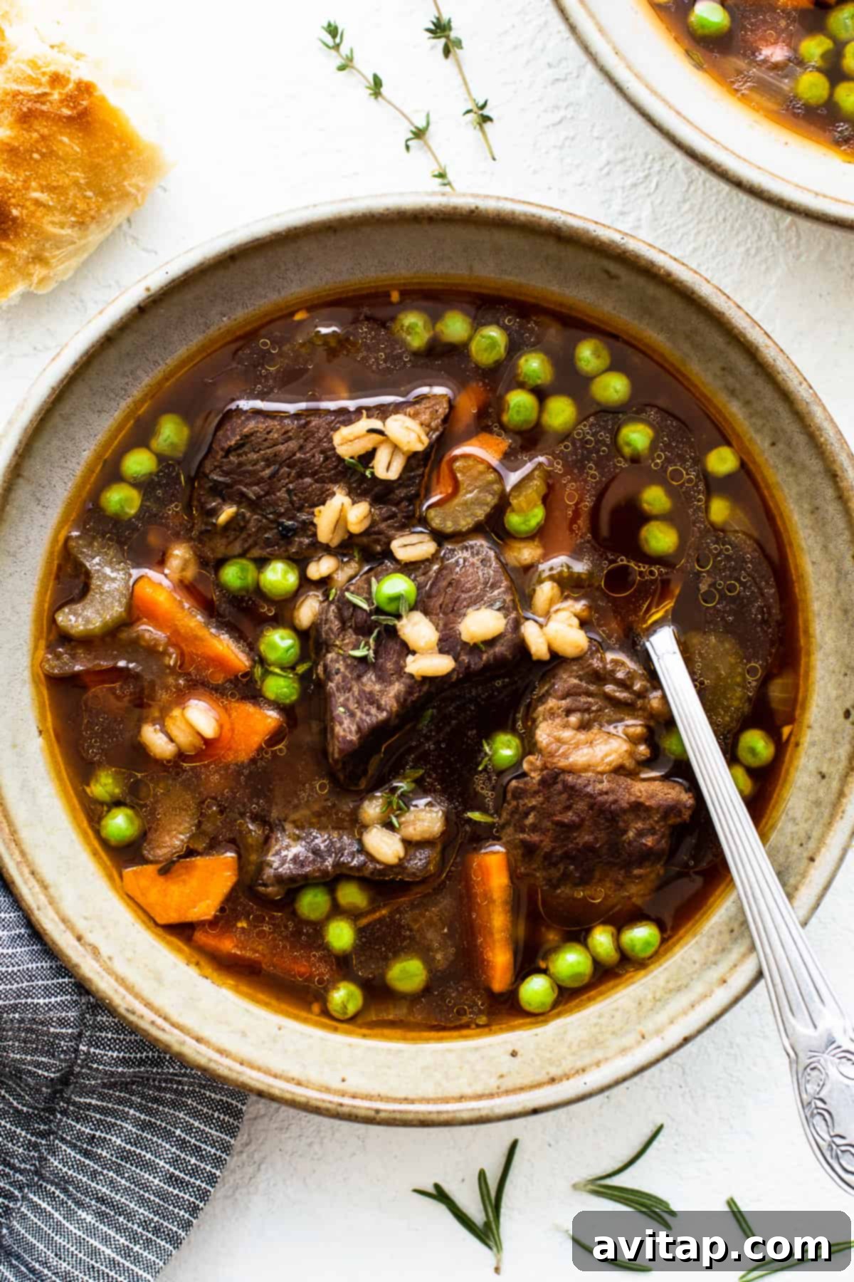 A steaming bowl of tender beef and barley soup, garnished with fresh herbs.