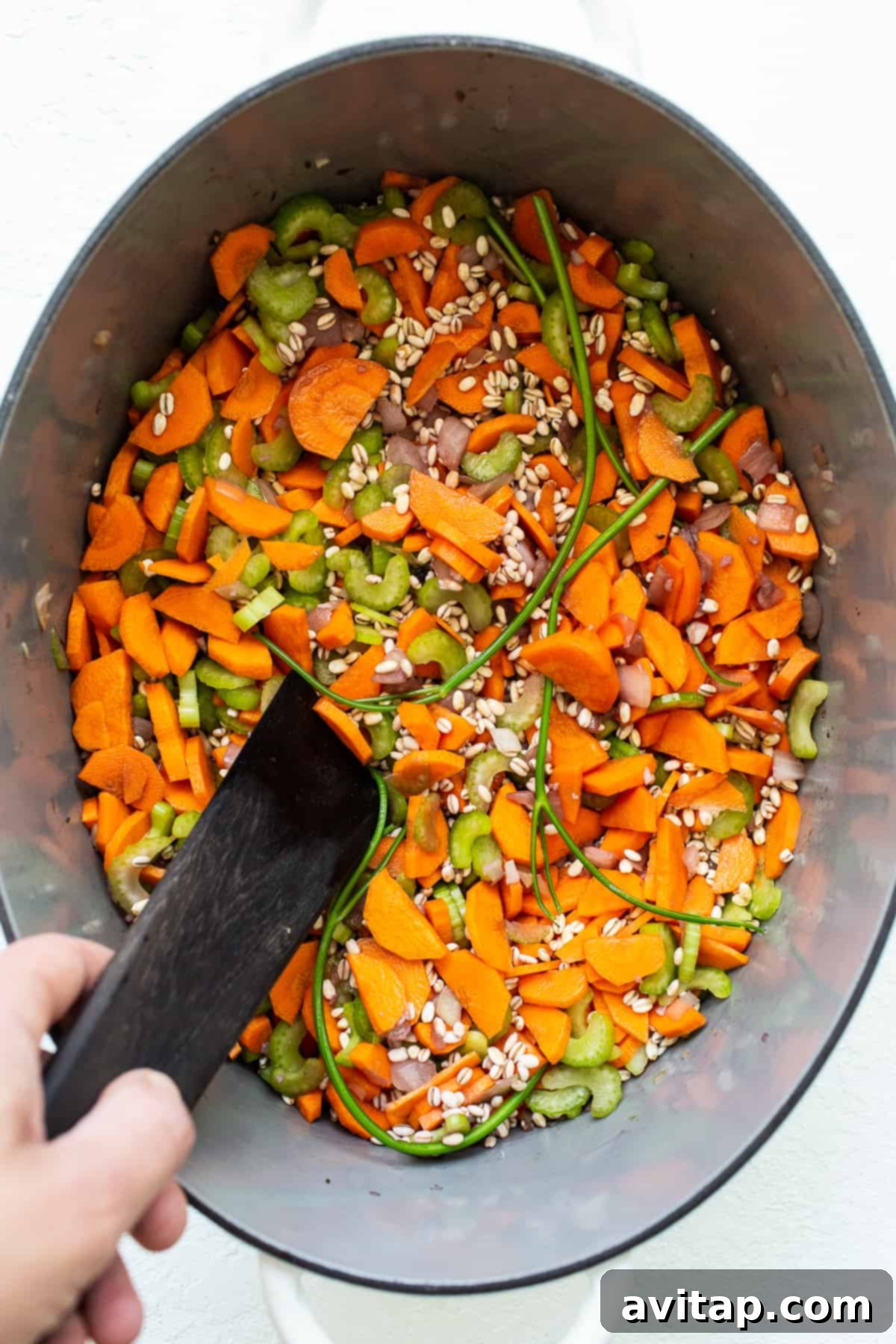 Colorful vegetables and pearl barley simmering in a rich broth within a Dutch oven.