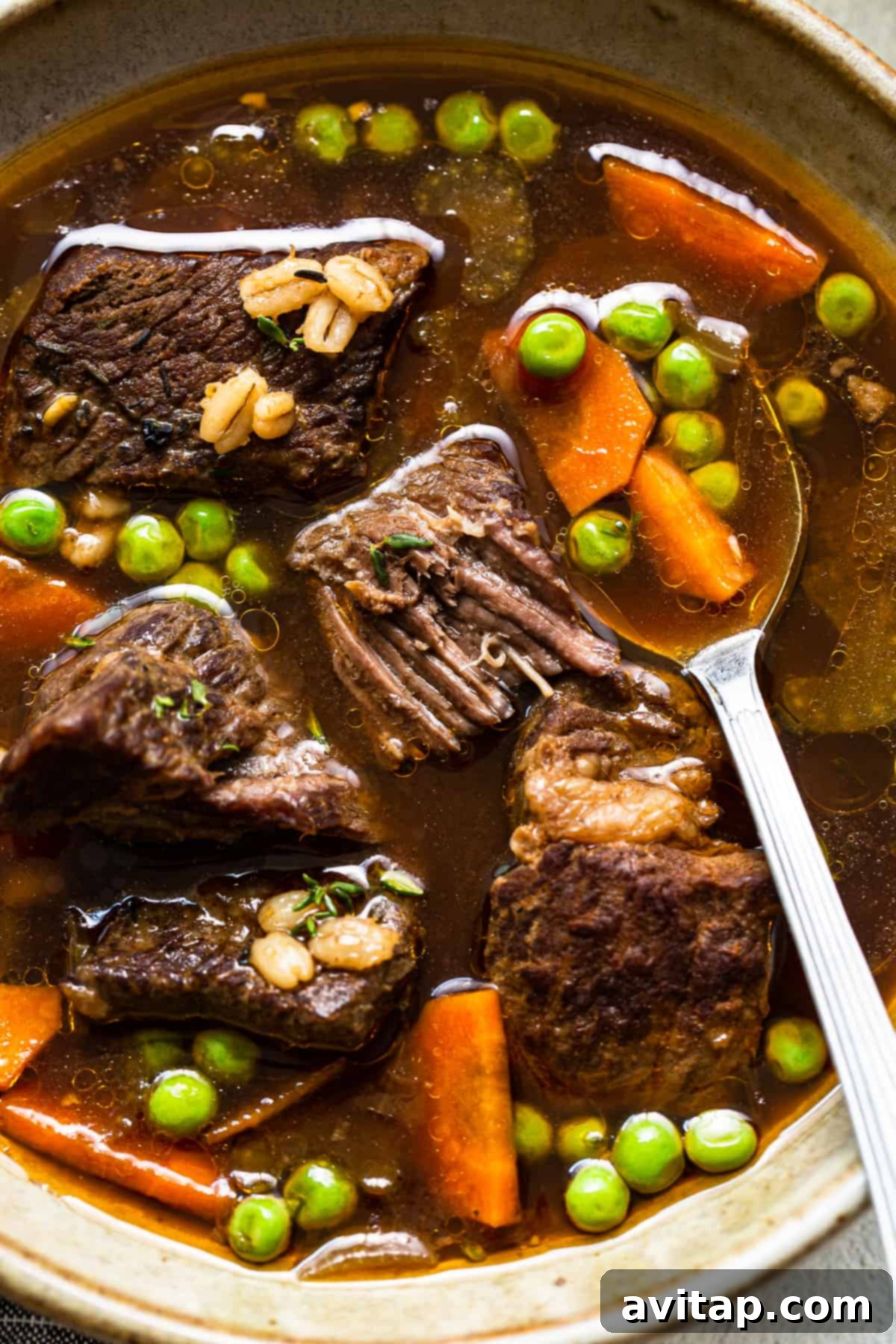 A generously filled bowl of hot beef and barley soup, ready to be enjoyed.