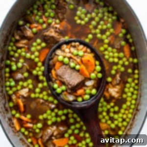 Hearty beef and barley soup simmering in a Dutch oven, with peas added.