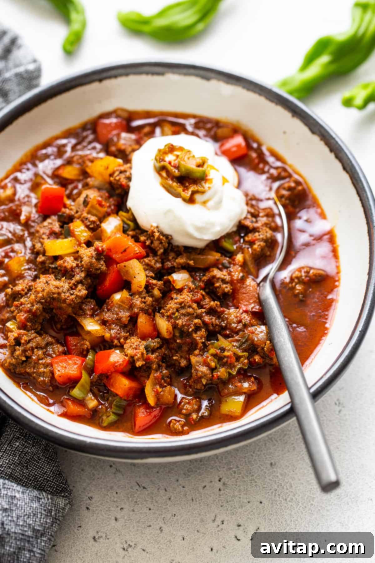 Texas chili in a bowl with a dollop of sour cream on top, garnished with green chilies.