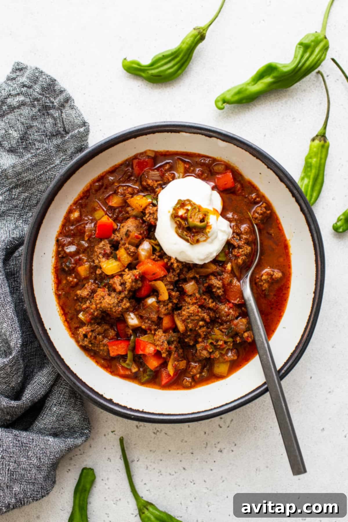 Texas chili in a bowl topped generously with sour cream and vibrant hatch chilies.