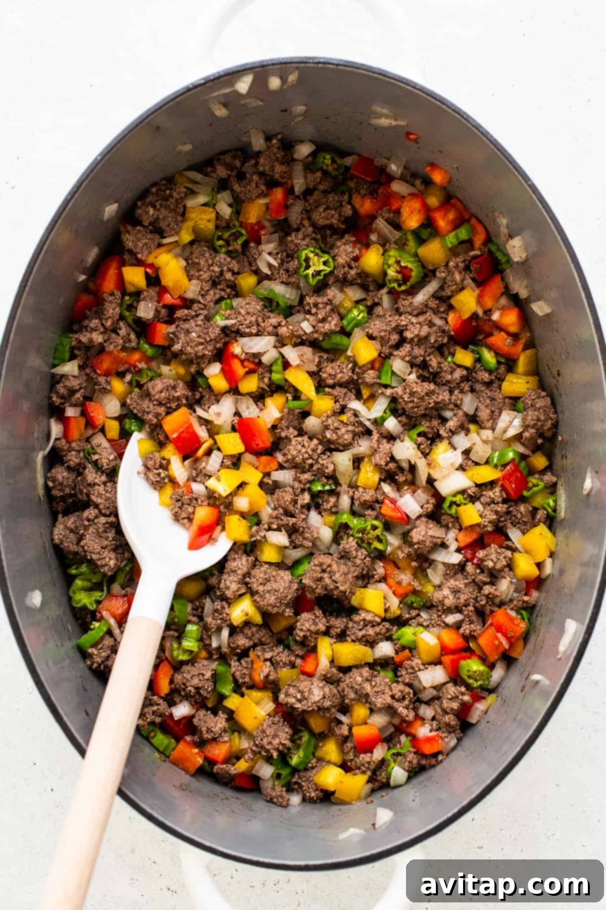 Ground beef, bell peppers, shishito peppers, and onion cooking in a large Dutch oven.