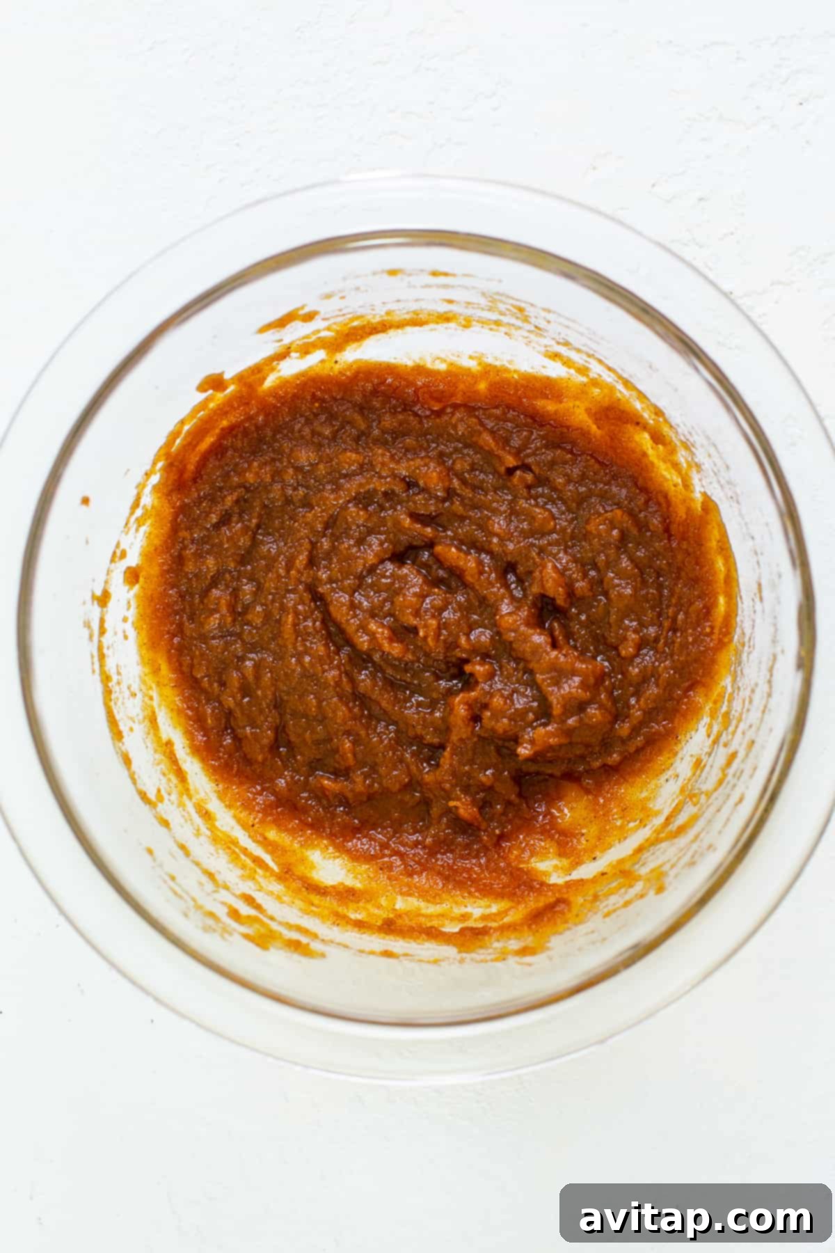 A smooth, orange pumpkin mixture for mousse in a white bowl, showcasing its creamy texture before being combined with whipped cream.
