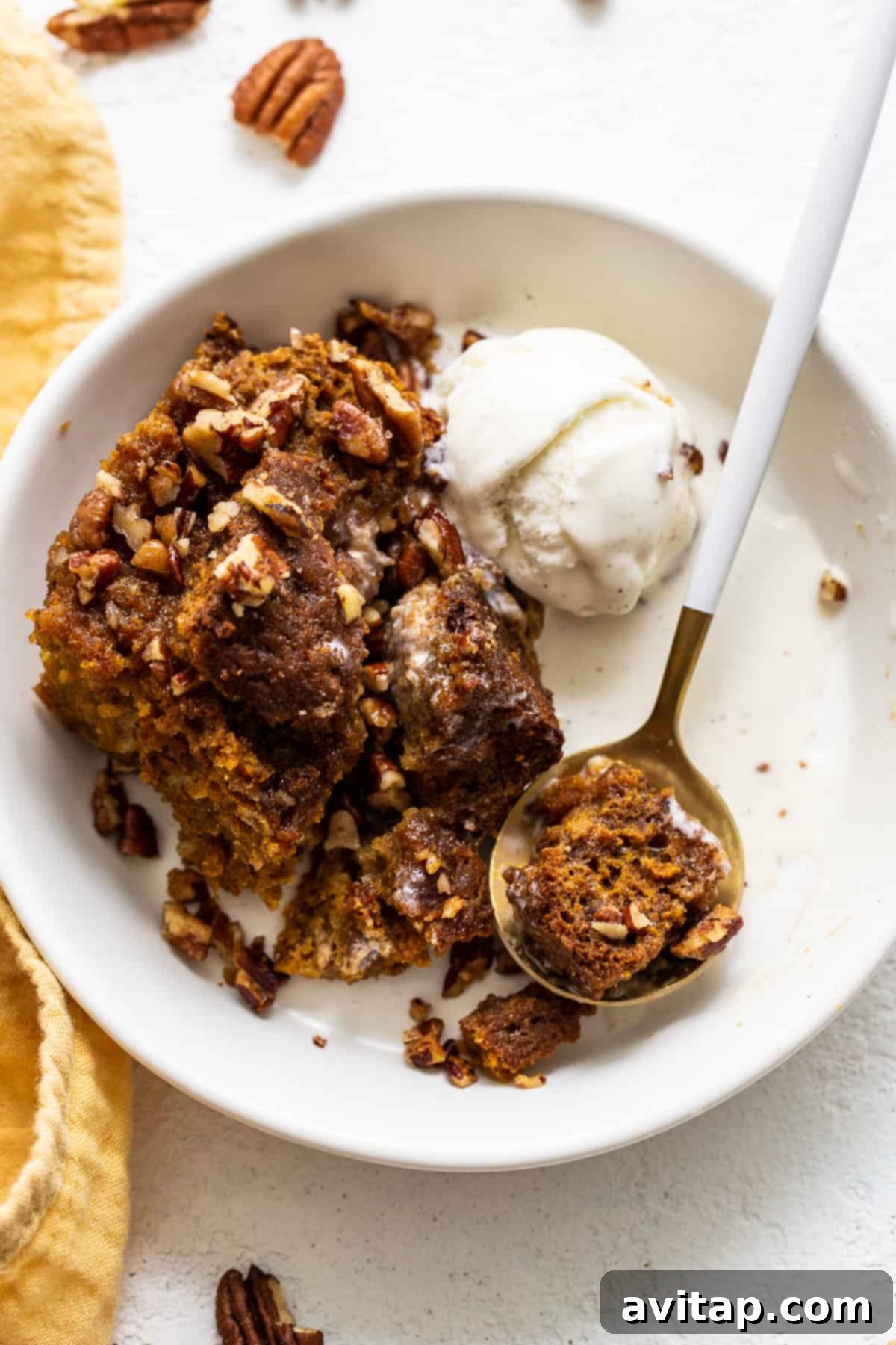 A bowl of pumpkin bread pudding topped with a melting scoop of vanilla ice cream, garnished with cinnamon.