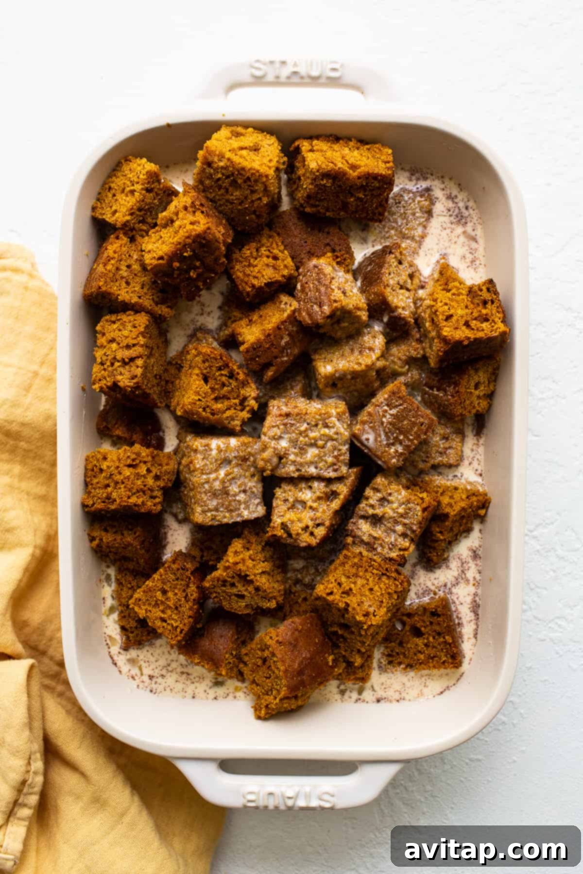 Cubed pumpkin bread soaking in a rich, spiced egg custard, preparing for baking into a delicious pudding.
