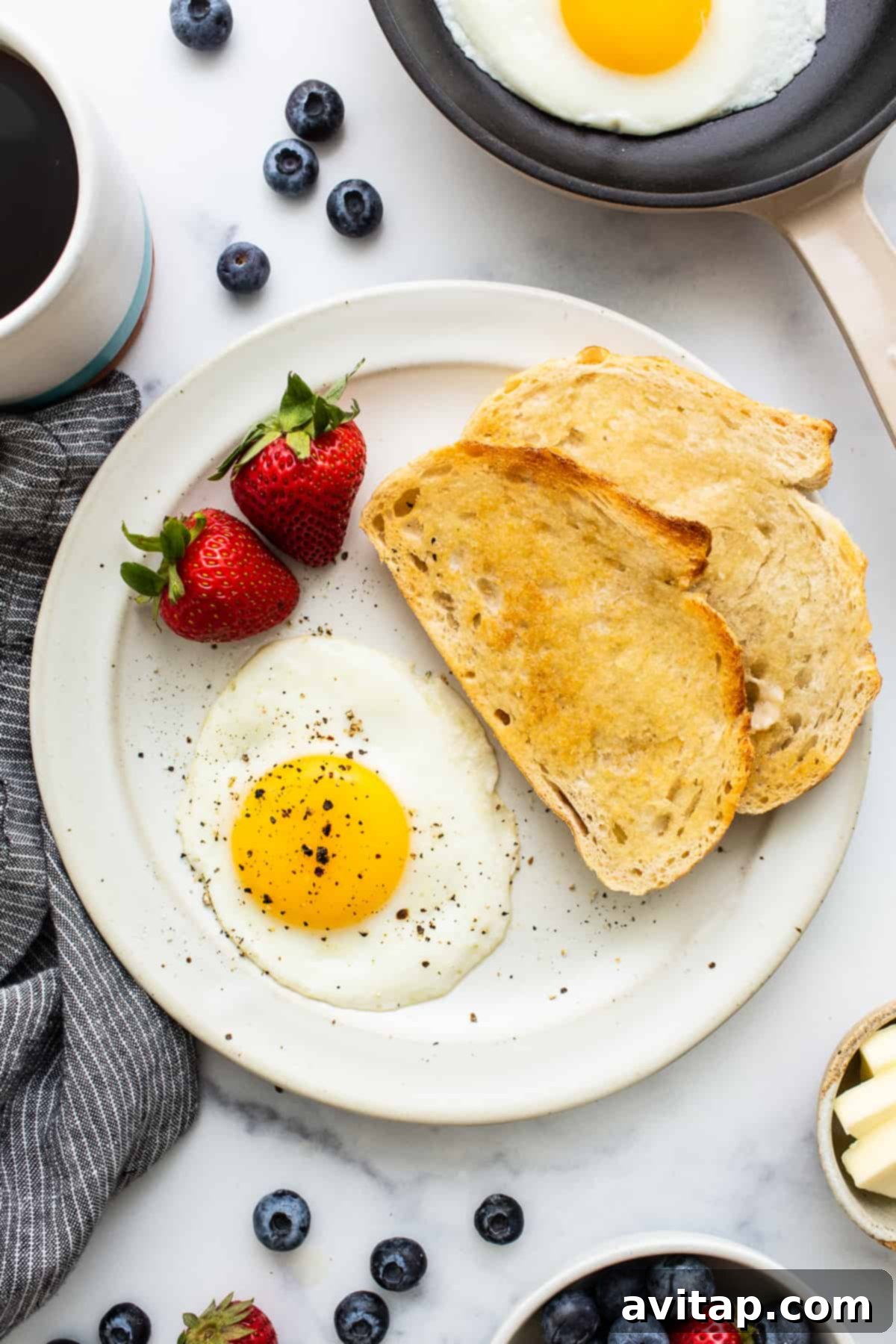 A perfectly cooked sunny side up egg on a plate, seasoned with salt and pepper.