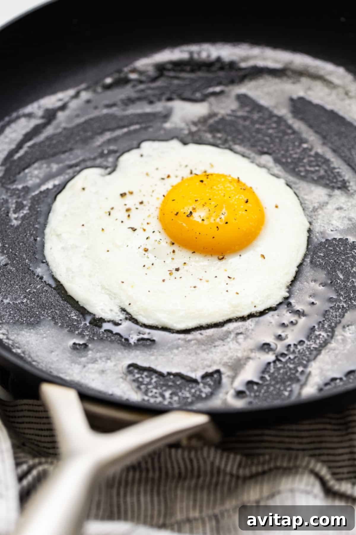 A close-up of an egg cooking in a pan, showing the setting whites and runny yolk.
