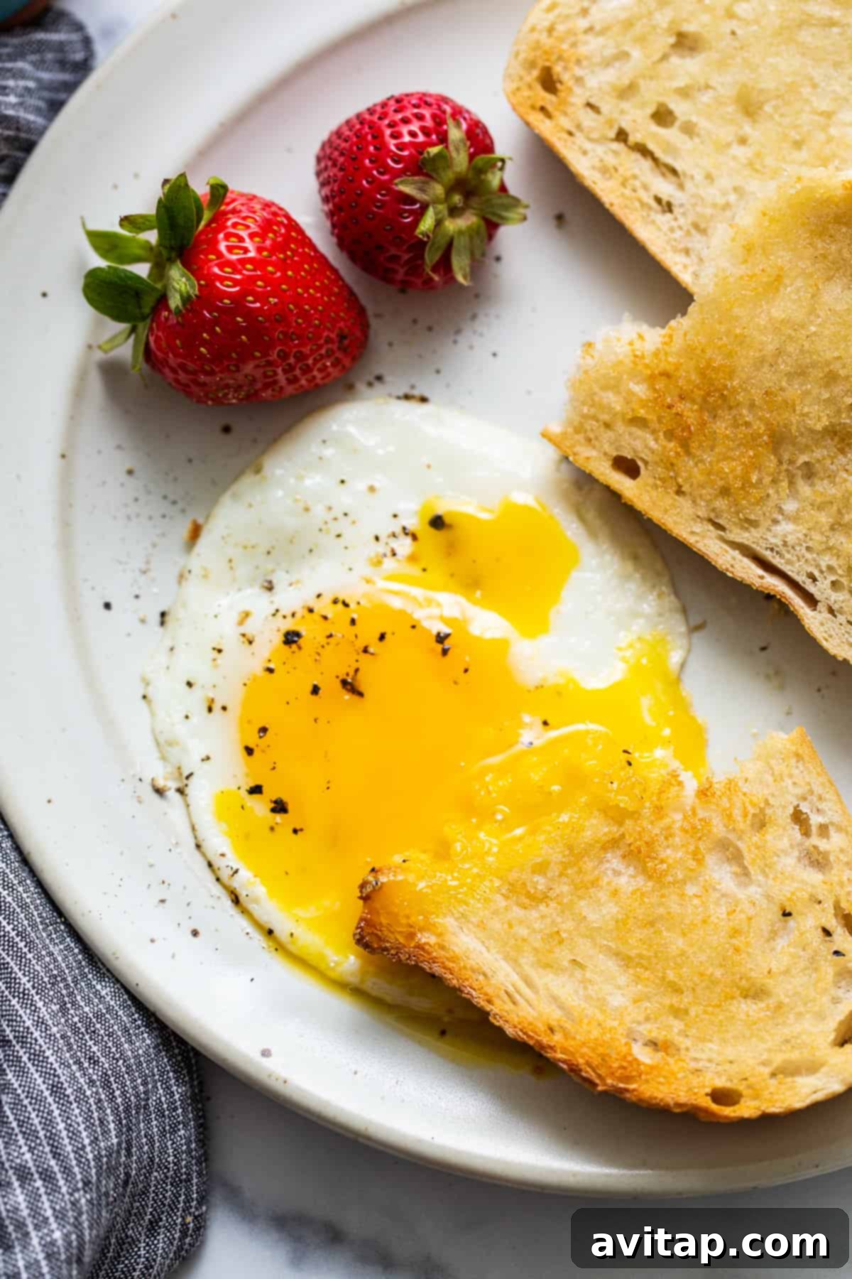 A perfect sunny side up egg with a runny yolk, served with a piece of buttered toast.