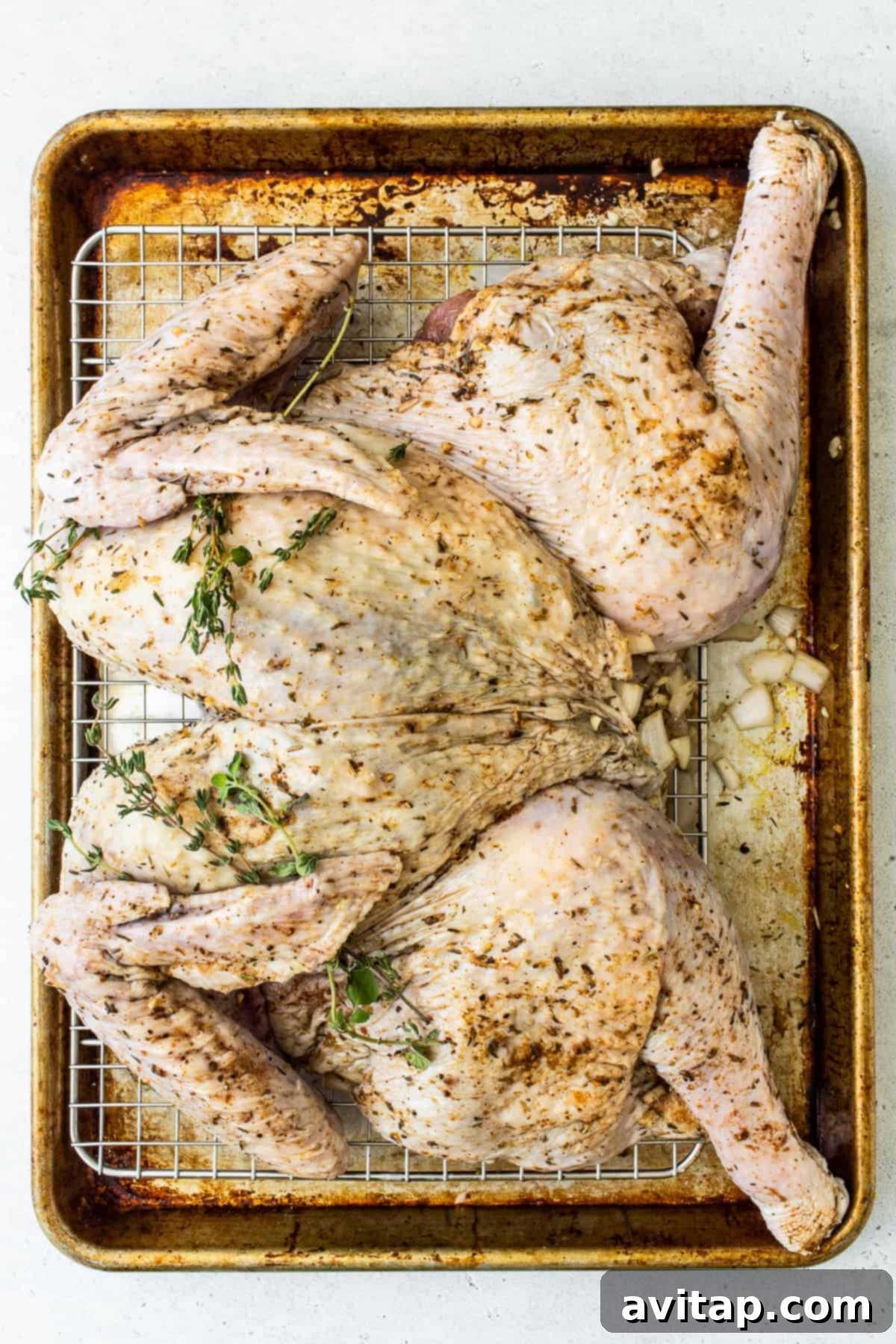Learn how to spatchcock a turkey and then roast it to perfection. This spatchcock turkey recipe leaves you with the juiciest herbed turkey meat and super crispy skin. Spatchcocked turkey on a baking sheet with fresh herbs tucked under the skin, ready for the oven.