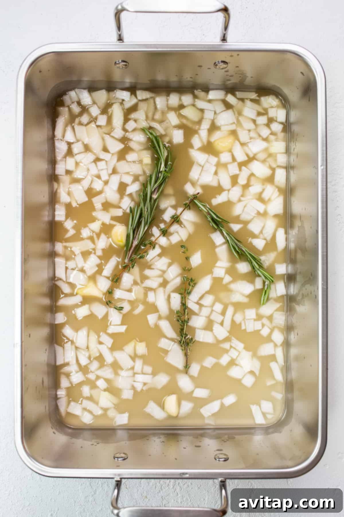 Rich basting liquid simmering in the bottom of a roasting pan, ready to moisturize the turkey.
