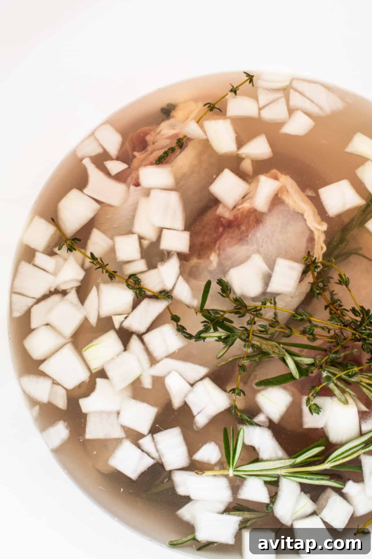A large bucket containing a whole turkey fully submerged in a vibrant, flavorful brine with visible onions, citrus slices, and fresh herbs.
