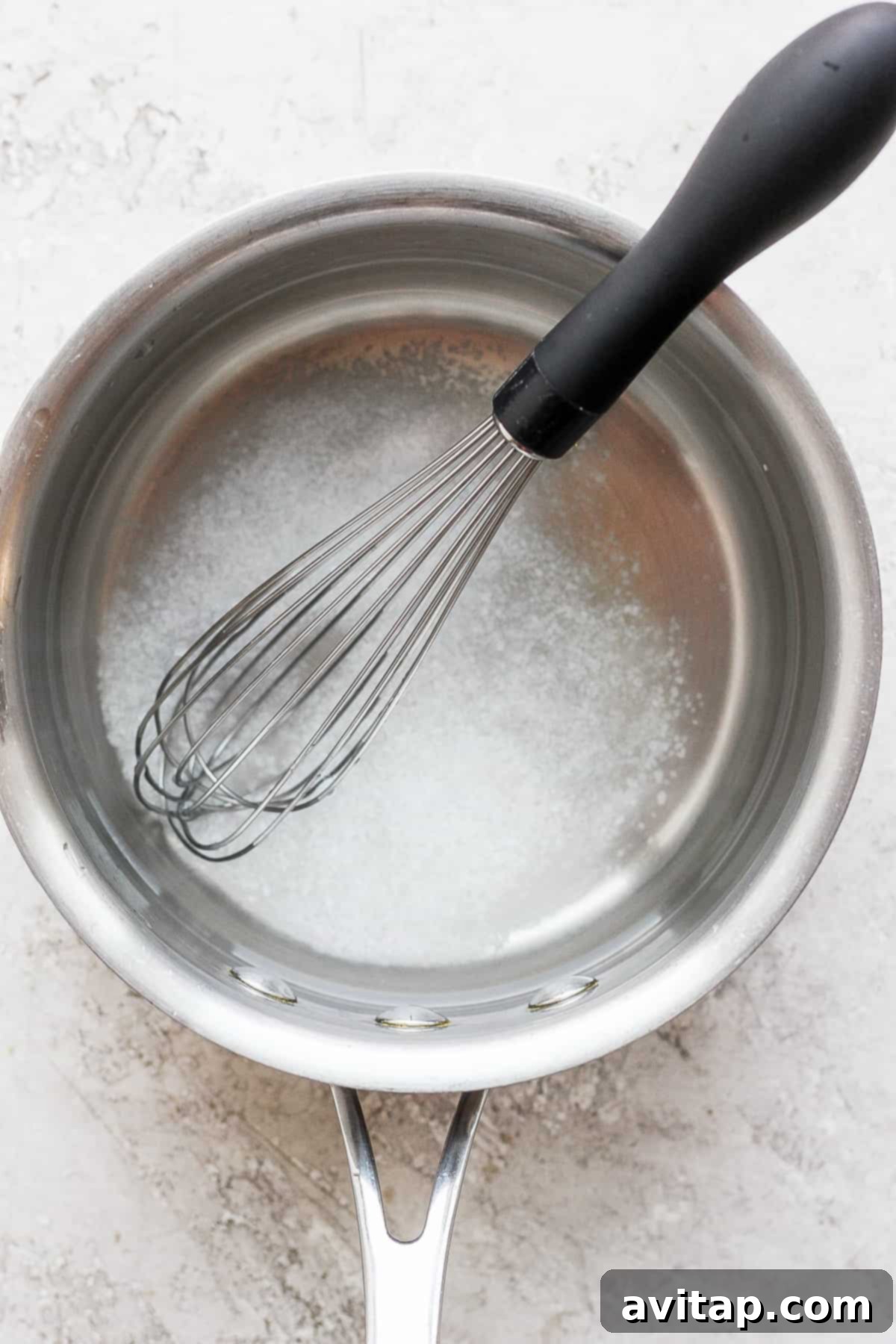 Kosher salt carefully dissolving into water in a saucepan over gentle heat, with a whisk nearby.