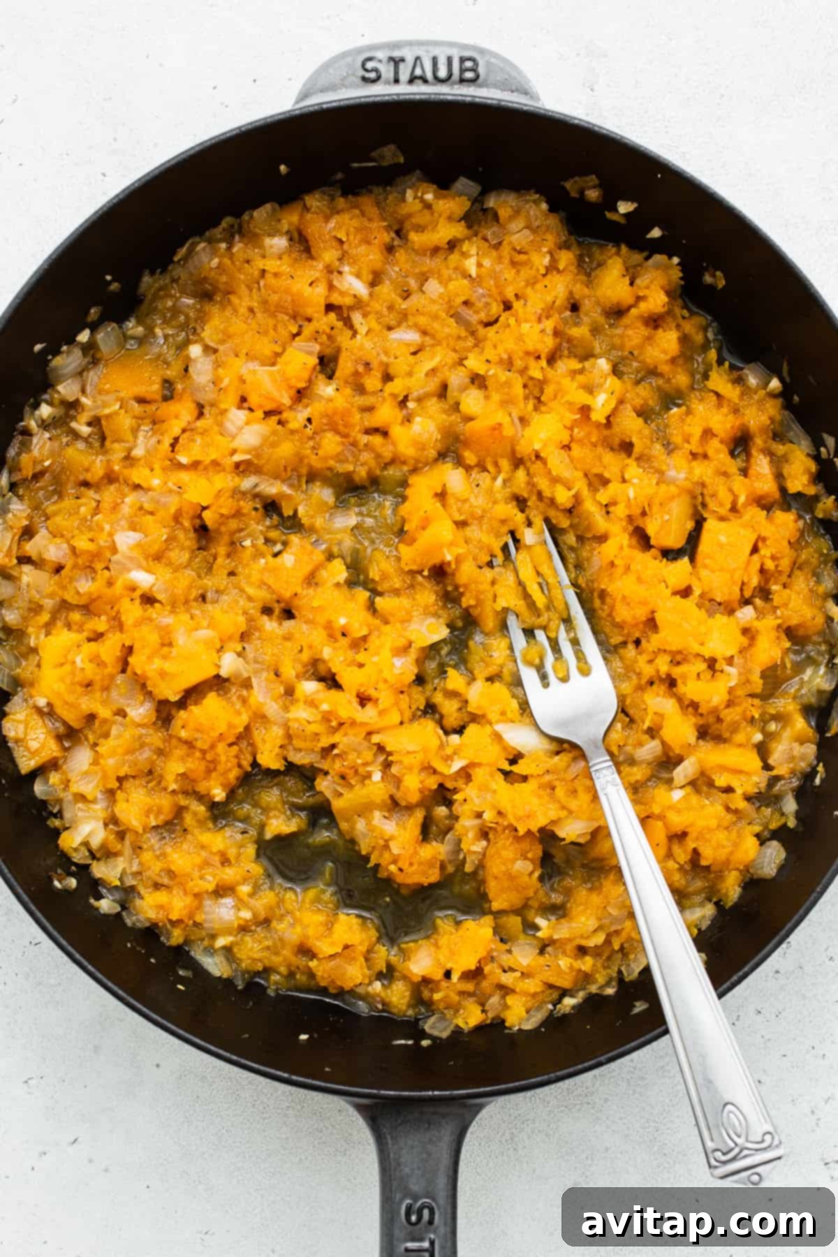 Individual ingredients for butternut squash risotto, including fresh sage, butternut squash cubes, and a bottle of white wine, arranged on a rustic wooden surface.