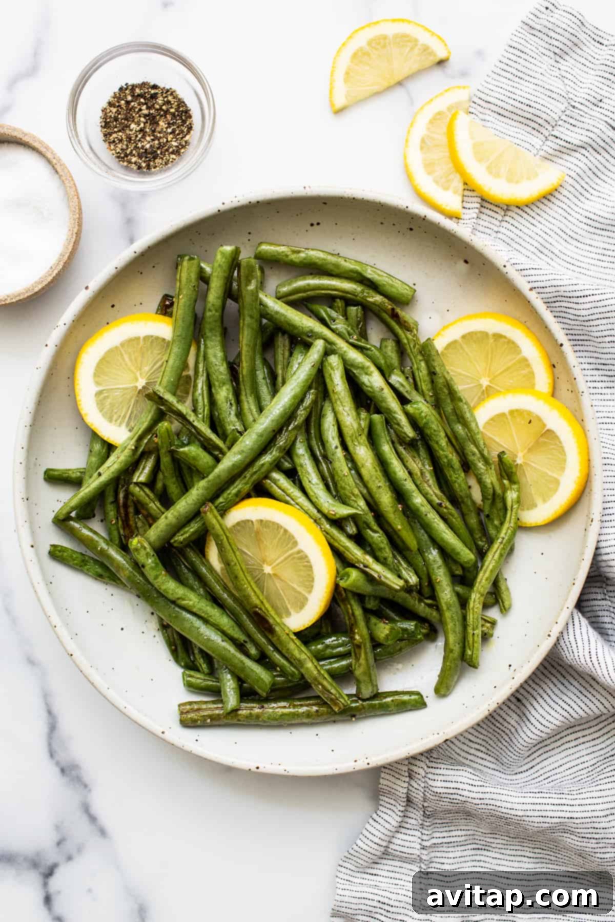 Vibrant roasted green beans elegantly arranged in a serving bowl, garnished with fresh lemon slices, ready to be enjoyed.