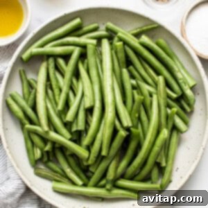 Trimmed green beans in a bowl, glistening with olive oil and seasoning.