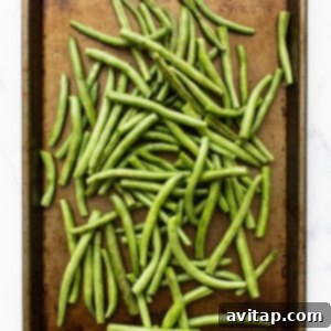 Roasted green beans actively cooking on a baking sheet, starting to brown and crisp.