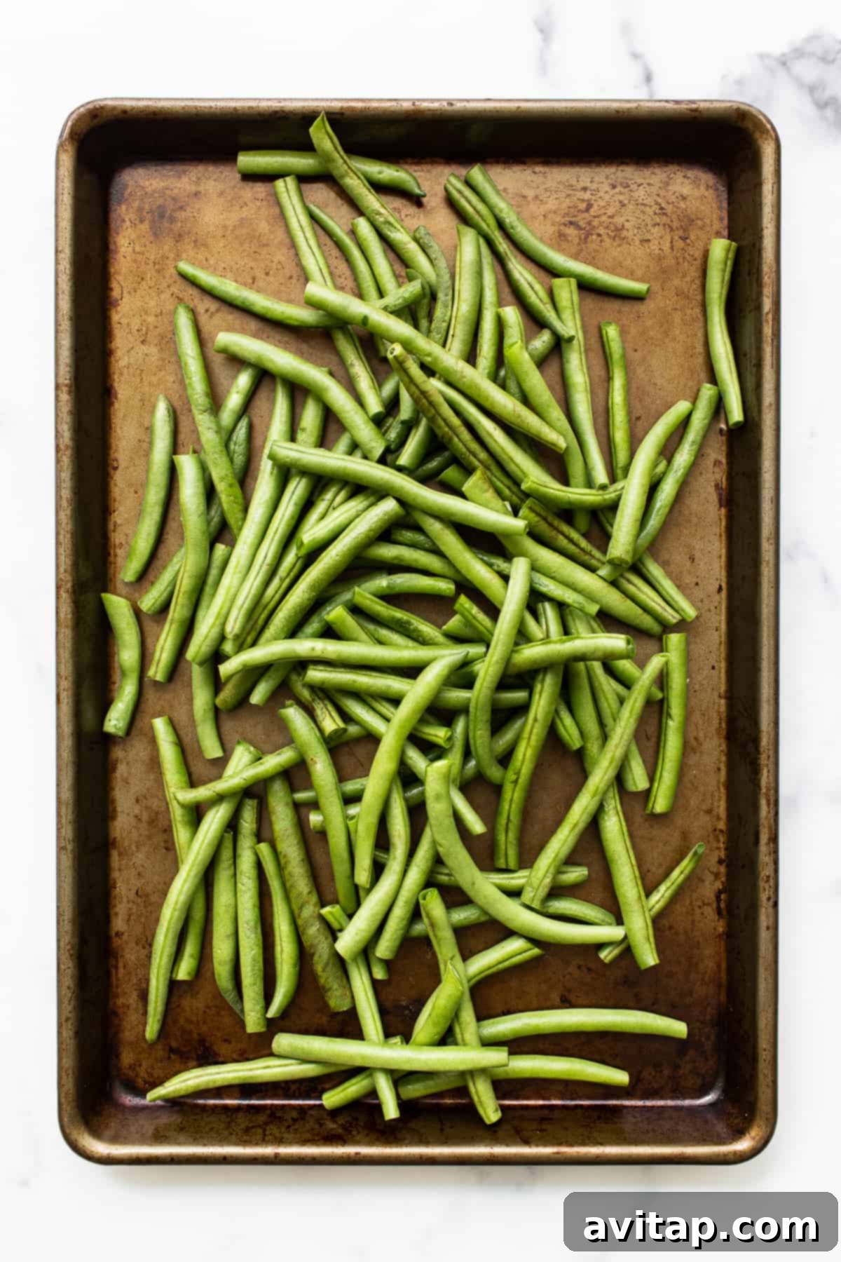 Fresh, uncooked green beans neatly spread on a baking sheet, ready for preparation.