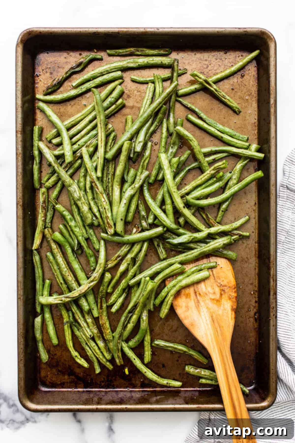 Beautifully roasted green beans spread out on a baking sheet, showing their crispy texture and slight char.