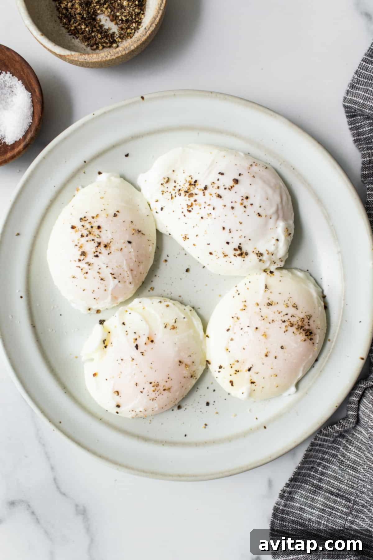 Flawless Poached Eggs Every Time 7 Four perfectly poached eggs neatly arranged on a white plate, seasoned with salt and pepper.