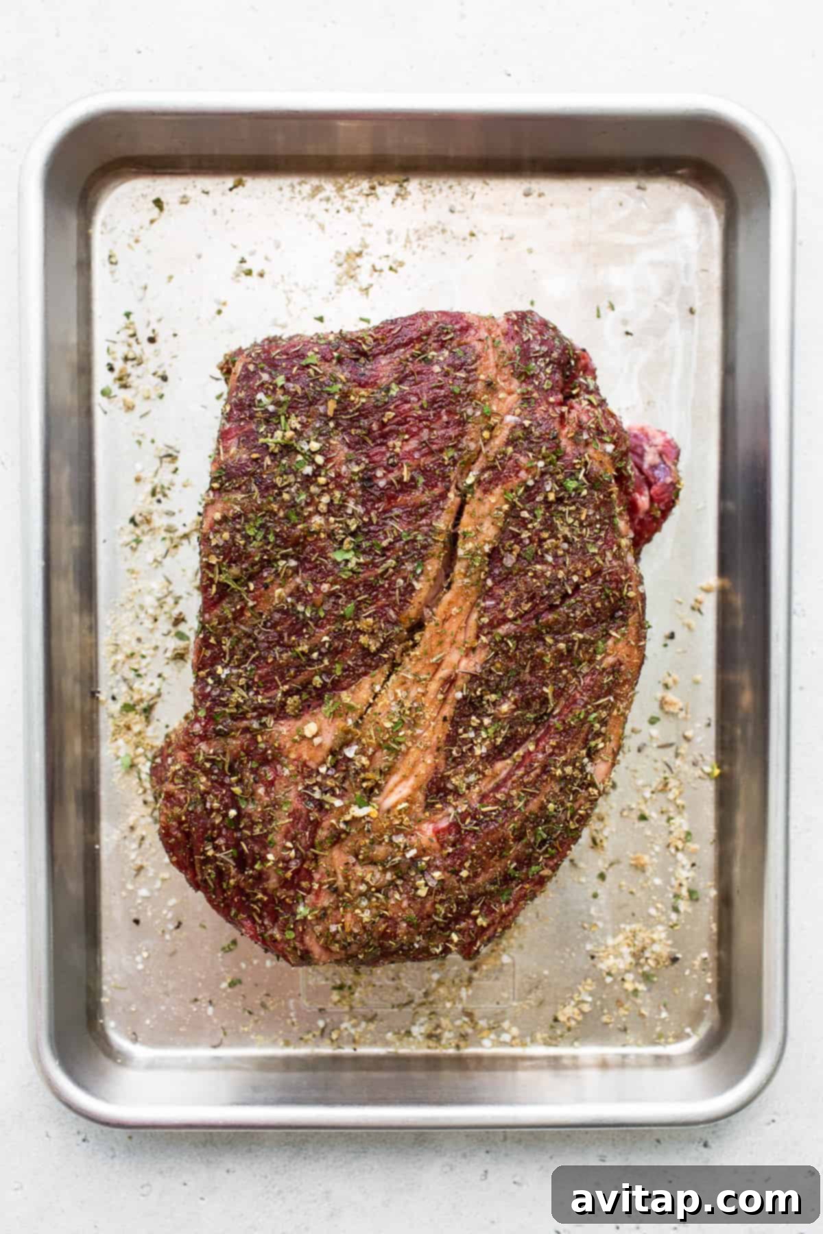 A raw boneless chuck roast resting on a baking sheet, ready for seasoning and preparation.
