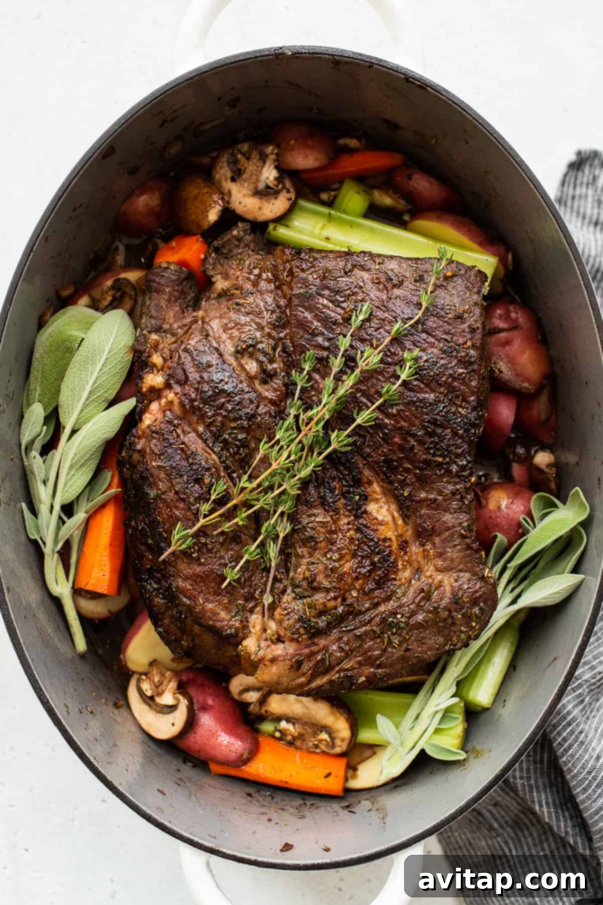 A beautifully cooked pot roast in a Dutch oven, generously topped with fresh herbs, ready to be served.