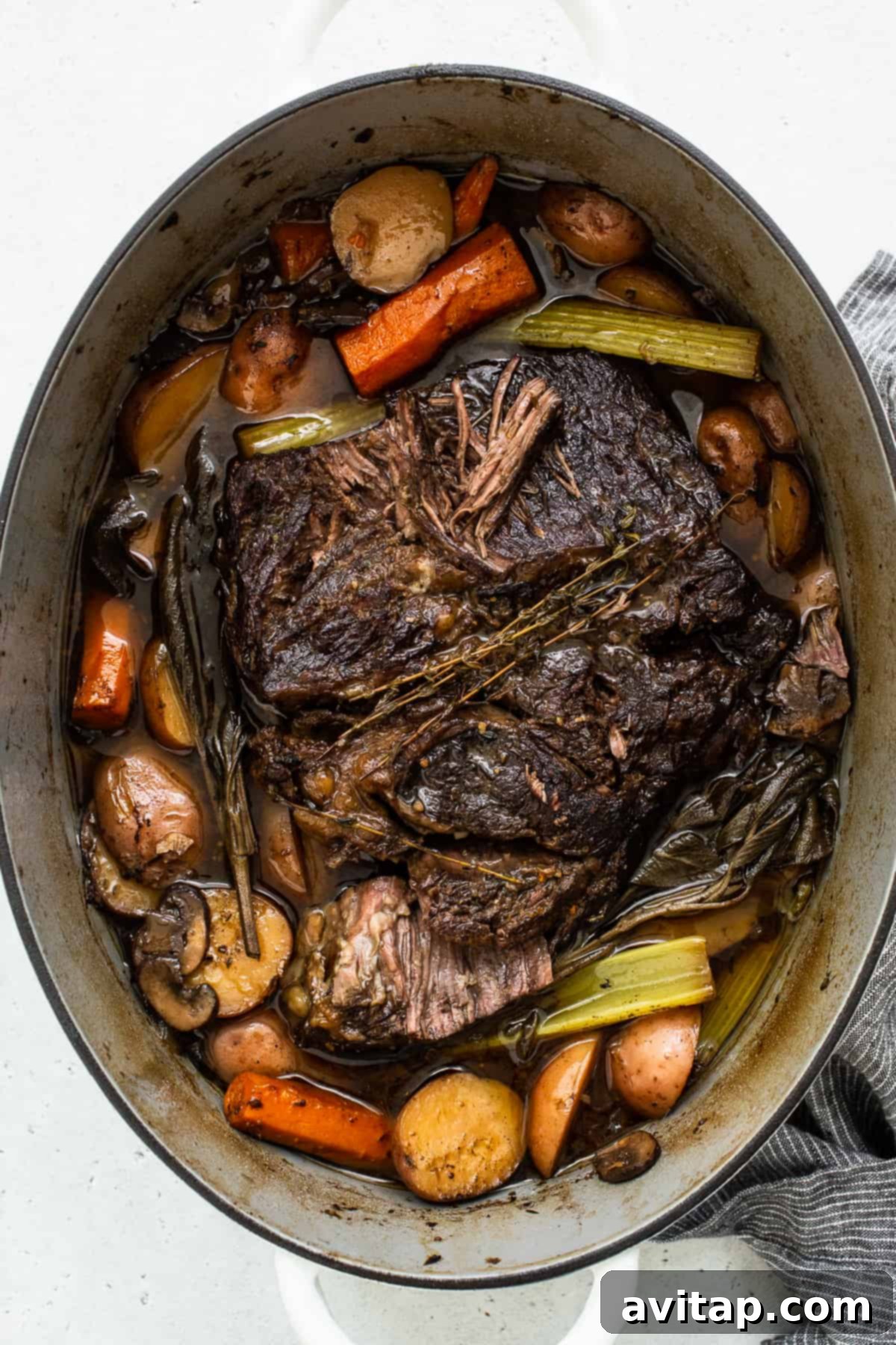 A fully cooked pot roast nestled in a Dutch oven, surrounded by tender carrots, potatoes, and celery, ready to be served.