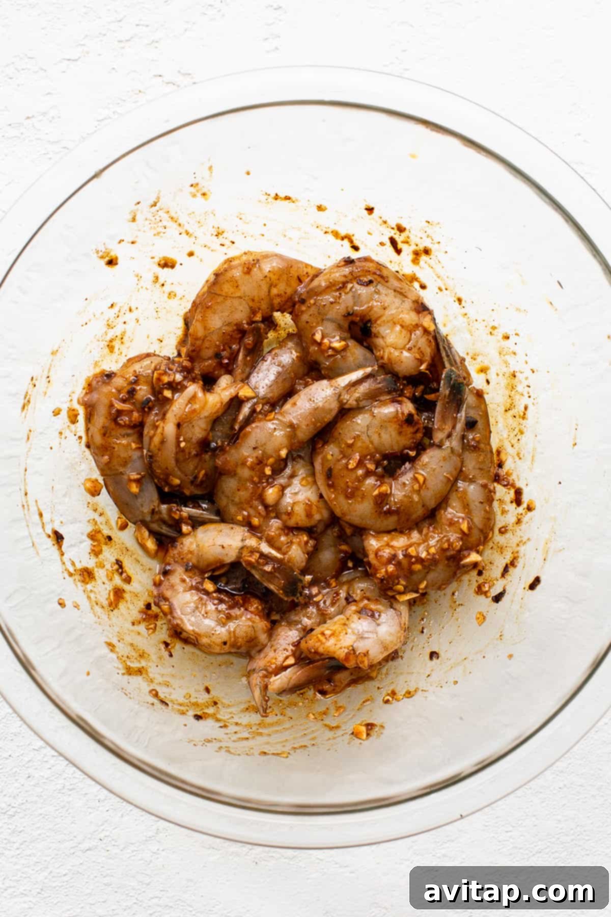 Raw jumbo shrimp sitting in a bowl, generously coated in a flavorful marinade, ready for the next step of preparation.