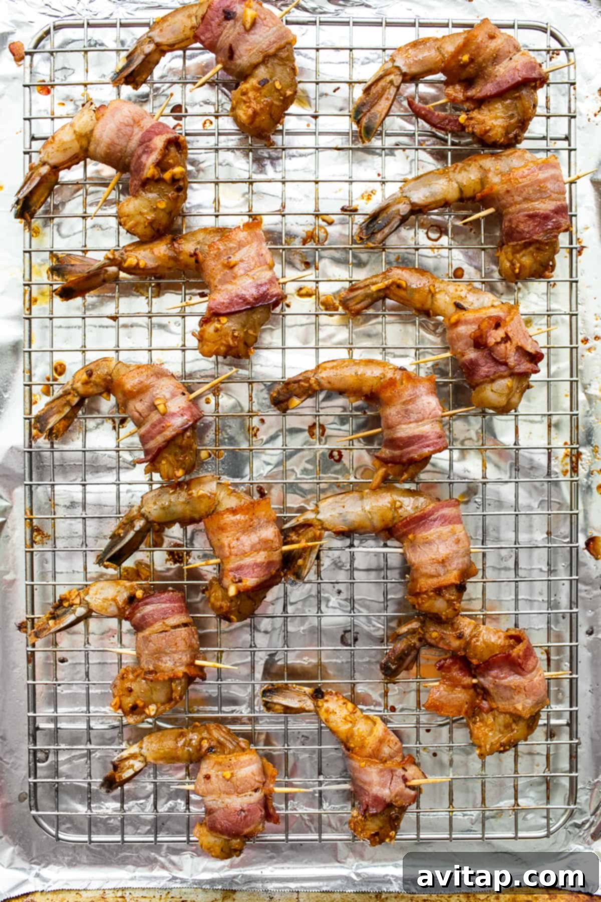 Partially cooked bacon wrapped shrimp skewered with toothpicks, neatly arranged on a baking sheet with a wire rack.