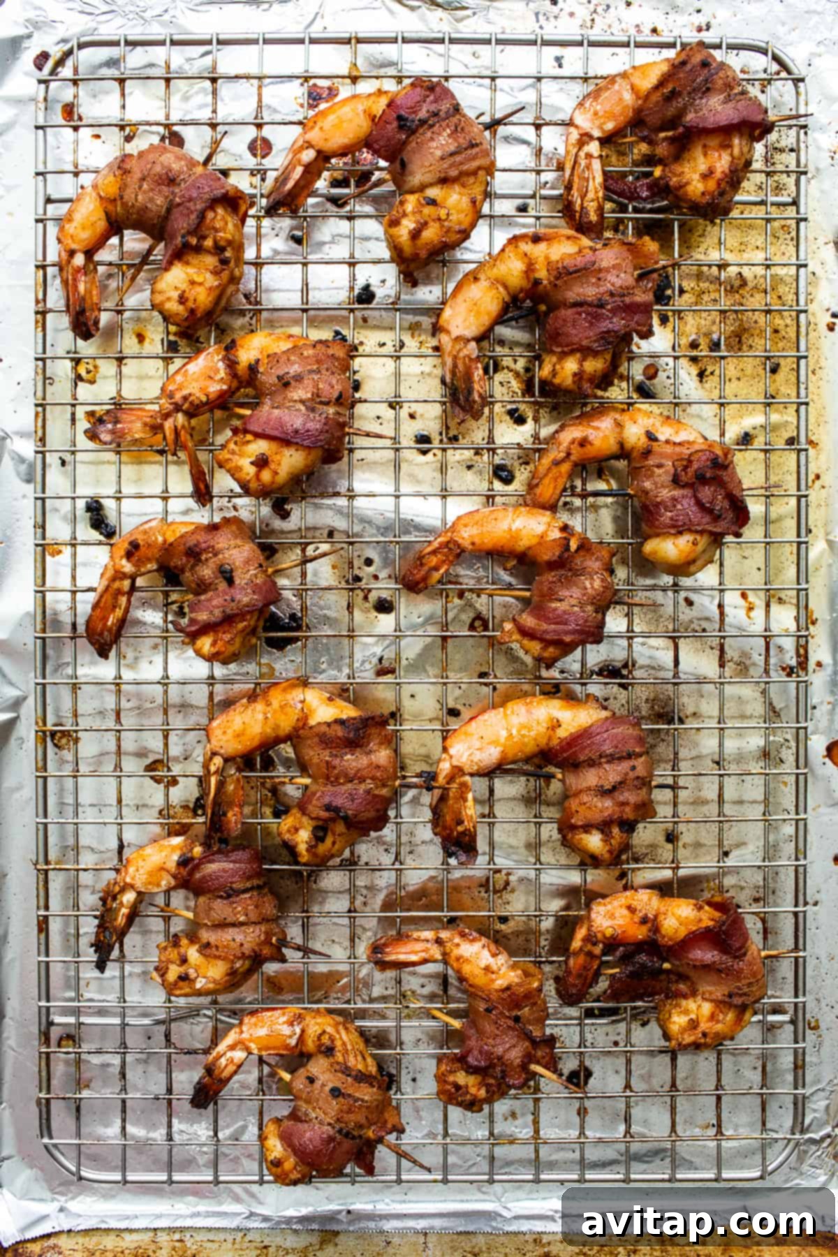 Freshly baked bacon wrapped shrimp on a baking sheet, glistening and golden, ready to be served hot.