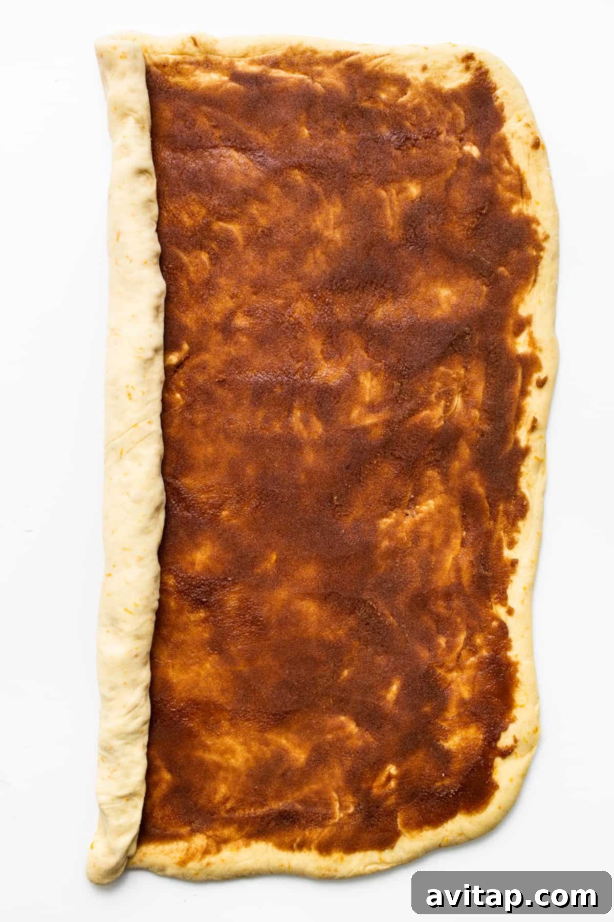 The process of rolling the sweet orange roll dough with a cinnamon-sugar filling spread evenly, showcasing the rich, spiced interior.