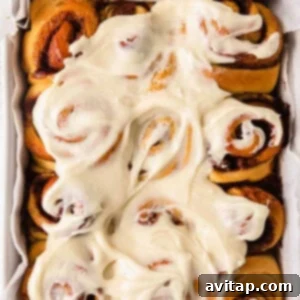 Close-up of fluffy maple cinnamon rolls topped with a generous swirl of maple cream cheese frosting, garnished with a dusting of cinnamon.