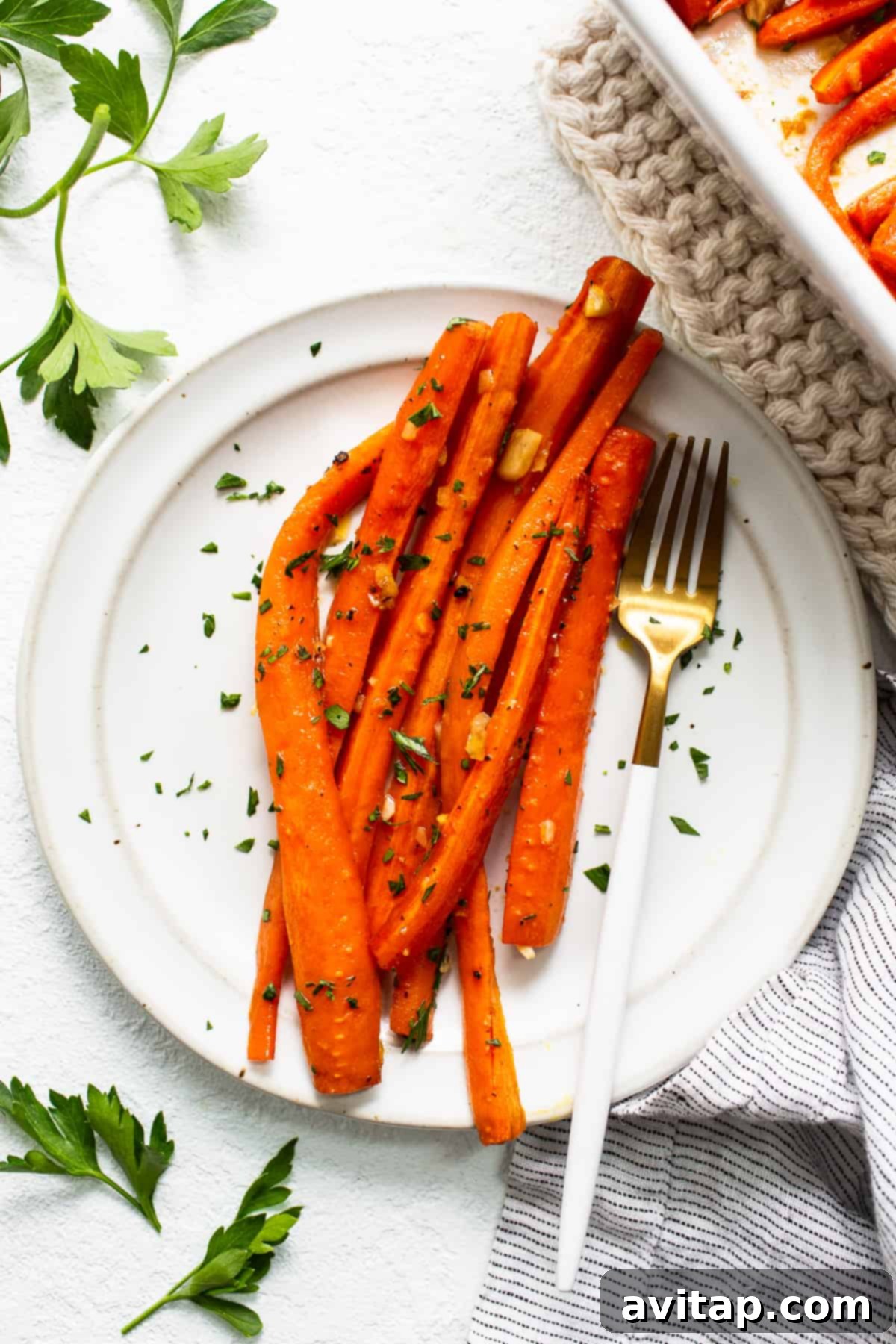 A fork taking a delicious bite of tender garlic glazed carrots from a white plate.