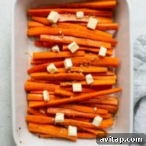 Sliced carrots in a white baking dish, seasoned and topped with butter before roasting.