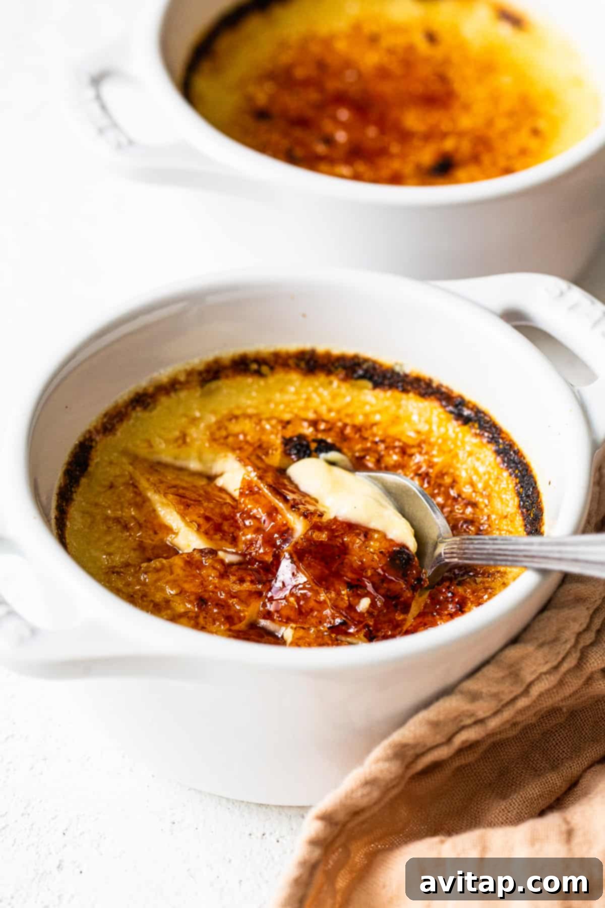 A spoon breaking through the caramelized sugar top of an Eggnog Creme Brûlée, revealing the creamy custard below.