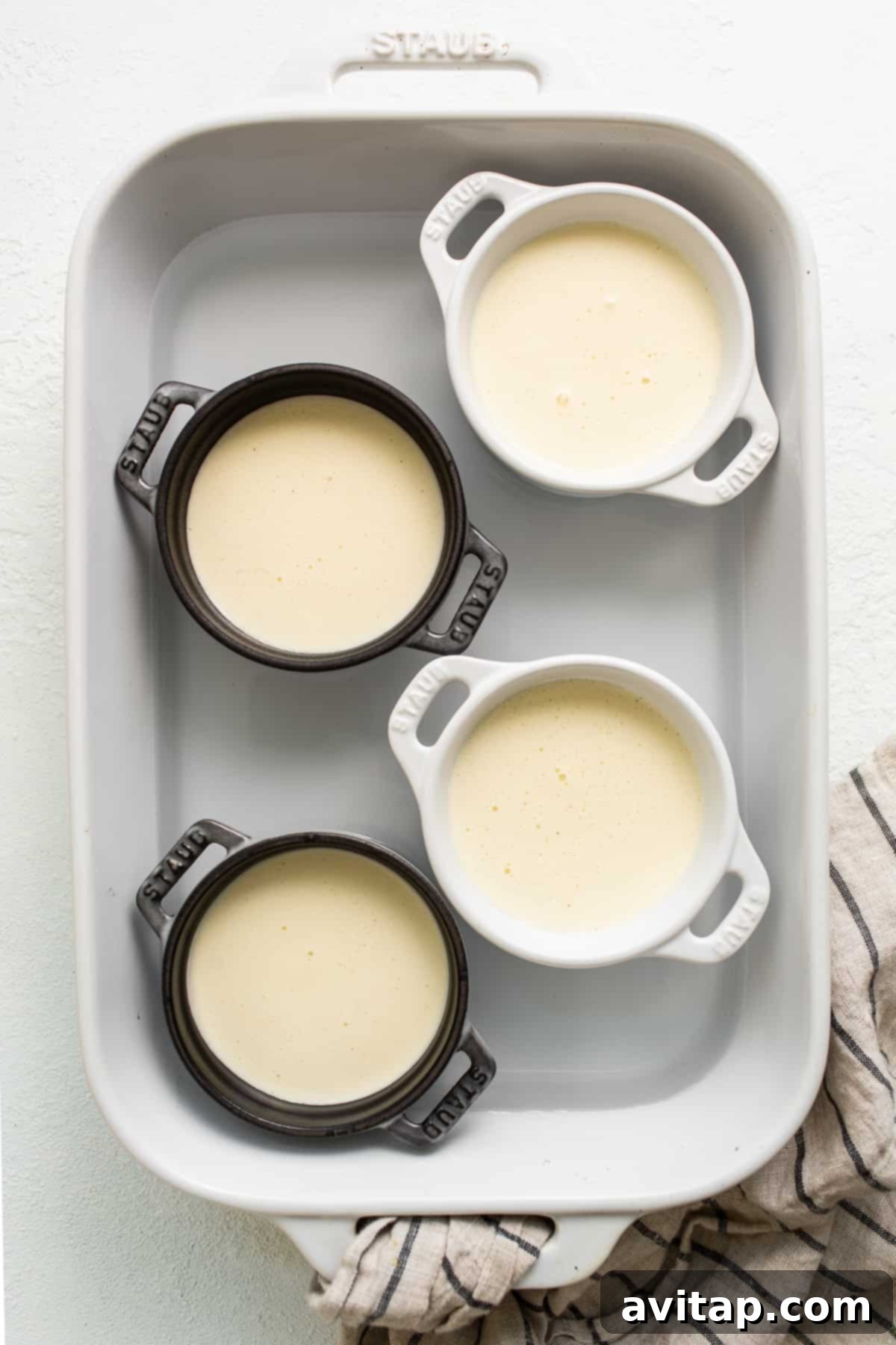 Four ramekins filled with the creamy eggnog ice cream mixture, ready for baking in a water bath.