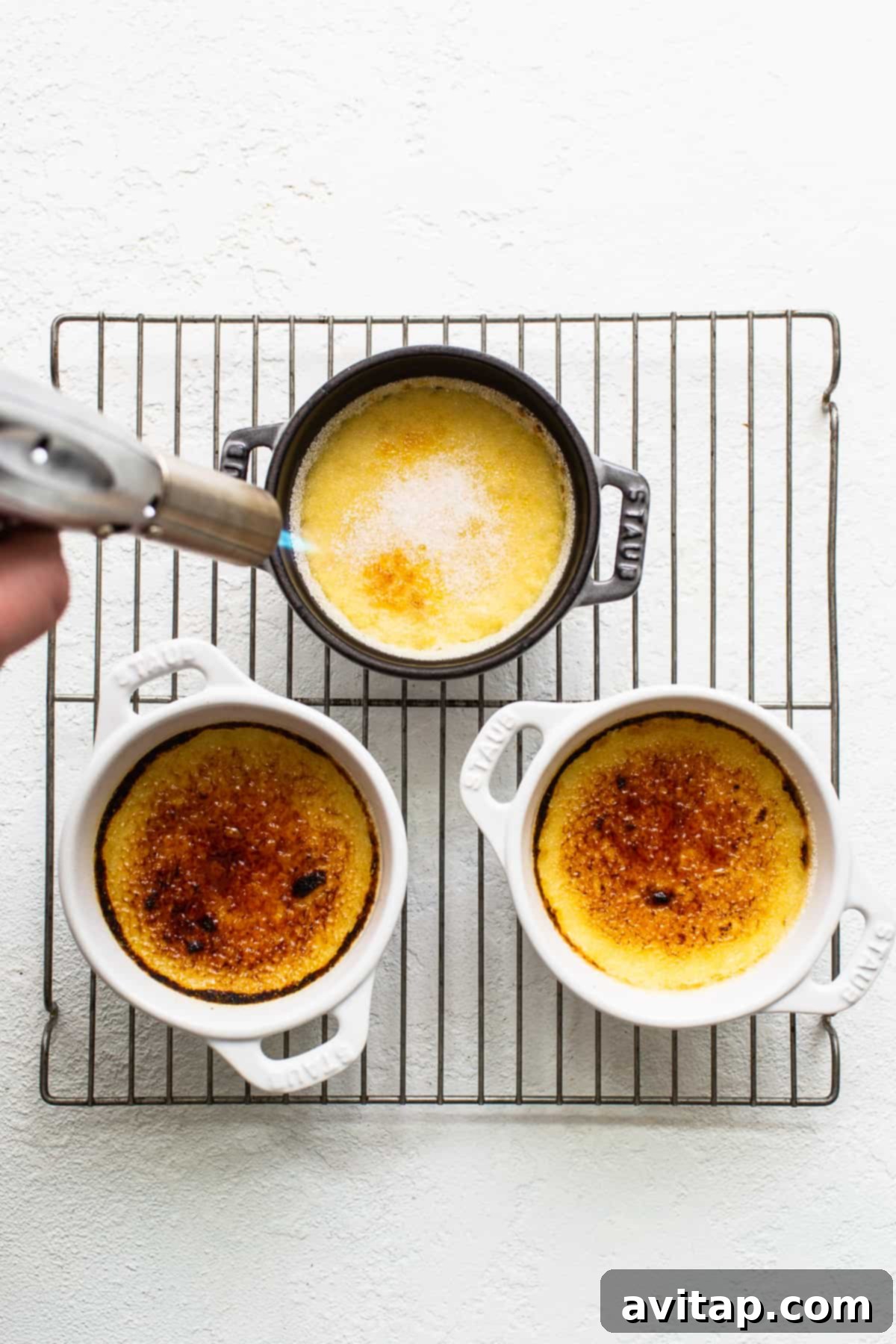 A kitchen torch caramelizing the sugar on top of an Eggnog Creme Brûlée, creating a crisp golden crust.