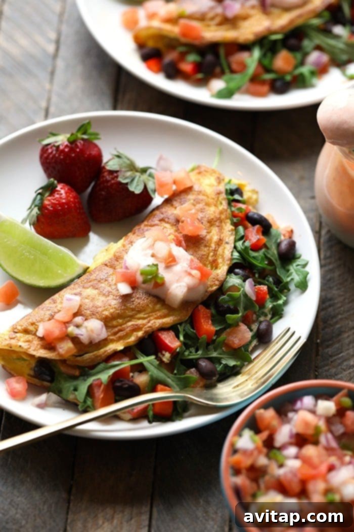 15 Delicious Breakfast Egg Recipes 19 A colorful veggie-packed black bean omelette, garnished with fresh avocado slices and served with strawberries.
