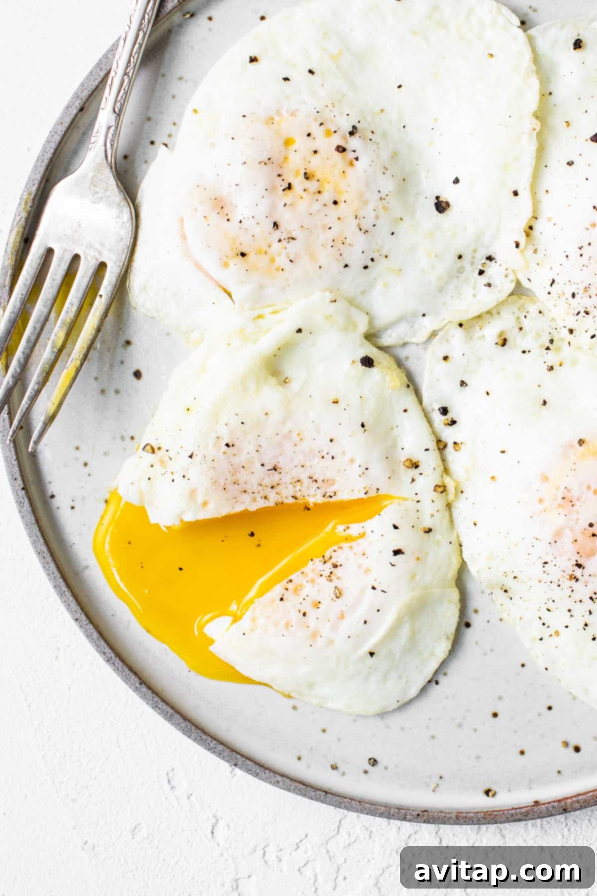 Achieve the perfect over easy eggs with a rich, runny yolk and tender whites. Over easy eggs on a plate with a fork, ready to be enjoyed.