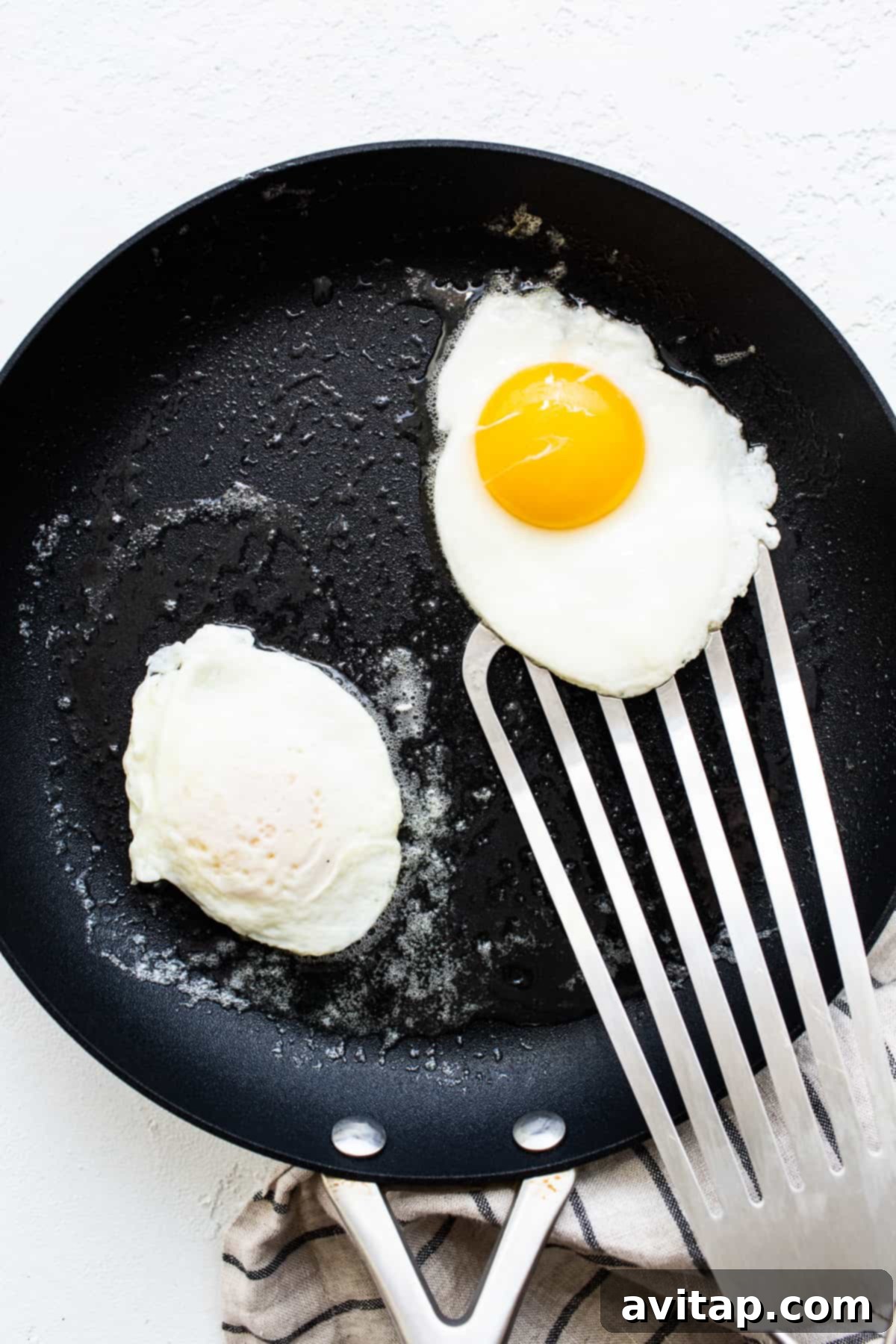 Observe the perfect moment to flip your over easy eggs. Two over easy eggs cooking in a skillet, nearly ready for flipping.