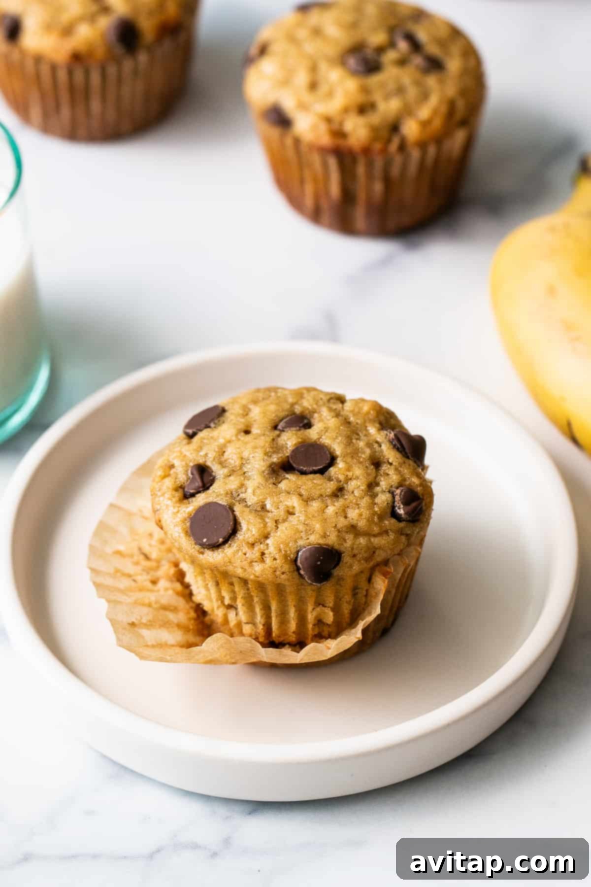 Single banana bread muffin. A single perfectly baked banana bread muffin on a clean white plate, showcasing its golden-brown exterior and inviting texture.