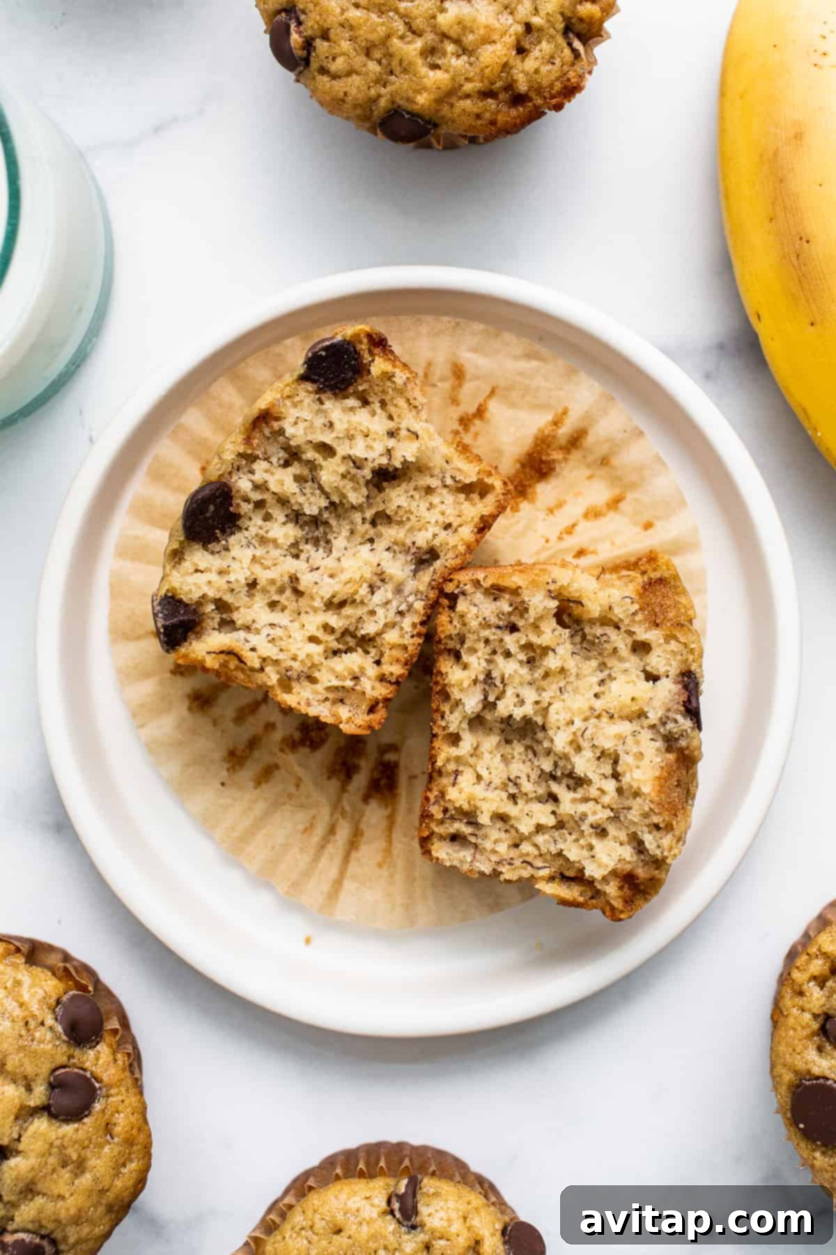 Banana bread muffin cut in half. A moist banana bread muffin, cut in half to reveal its tender, fluffy interior with hints of banana, resting on a small white plate.